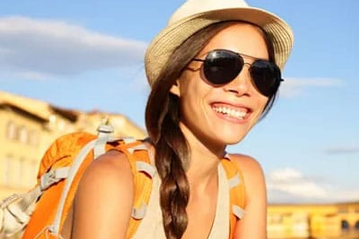 Woman sitting outside smiling wearing sunglasses.