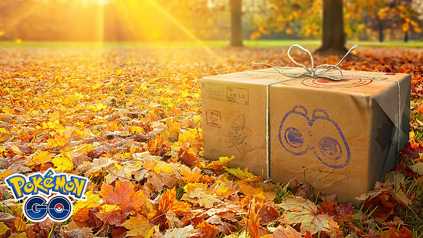 A box wrapped in kraft paper and twine sits on a layer of red, orange, and yellow leaves covering the ground. The Pokemon Go logo is at bottom-left.