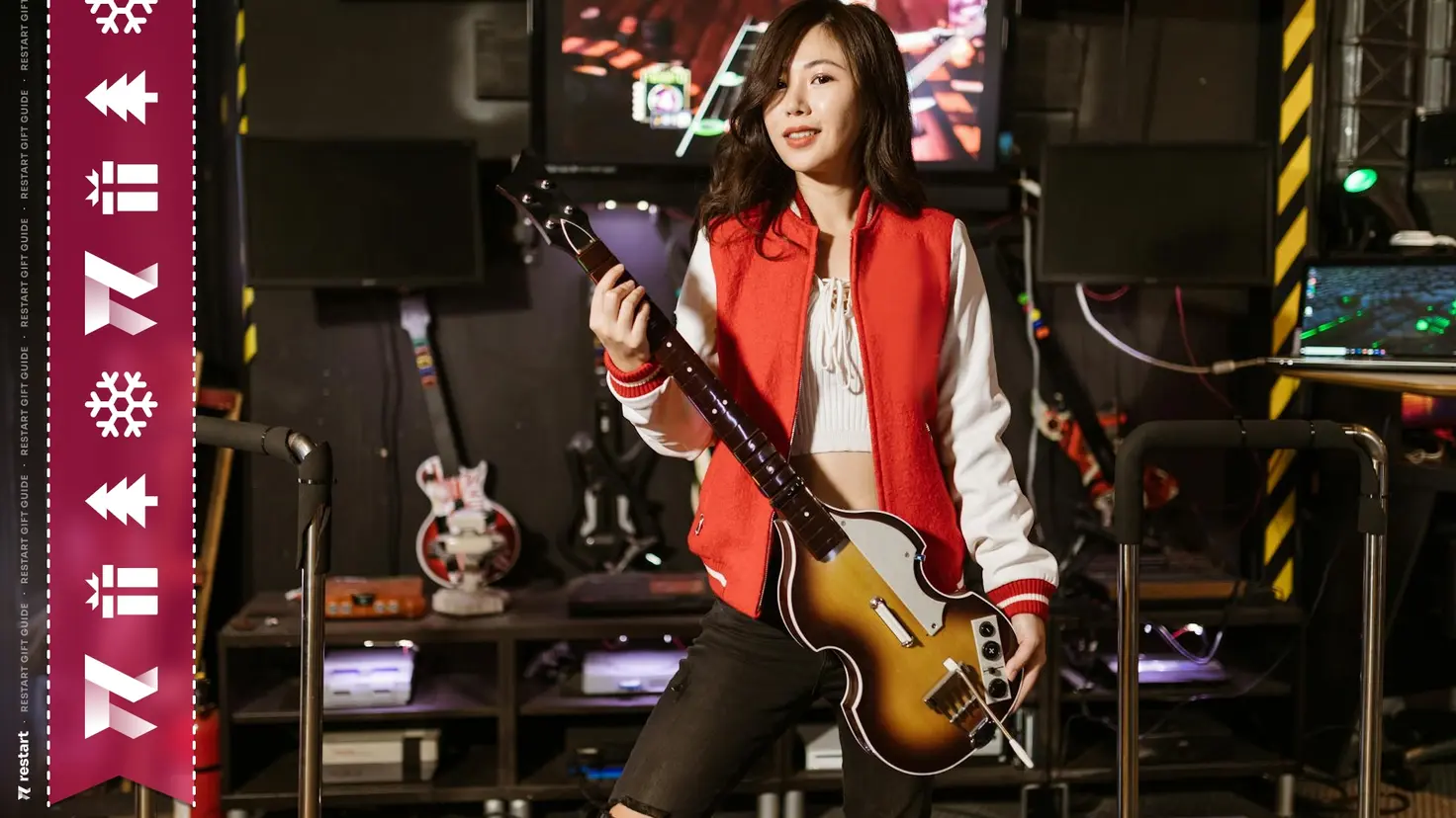 A woman stands holding a guitar controller for Rock Band, it's the Beatles special edition version styled after Paul McCartney's Hofner 500/1 bass guitar. 