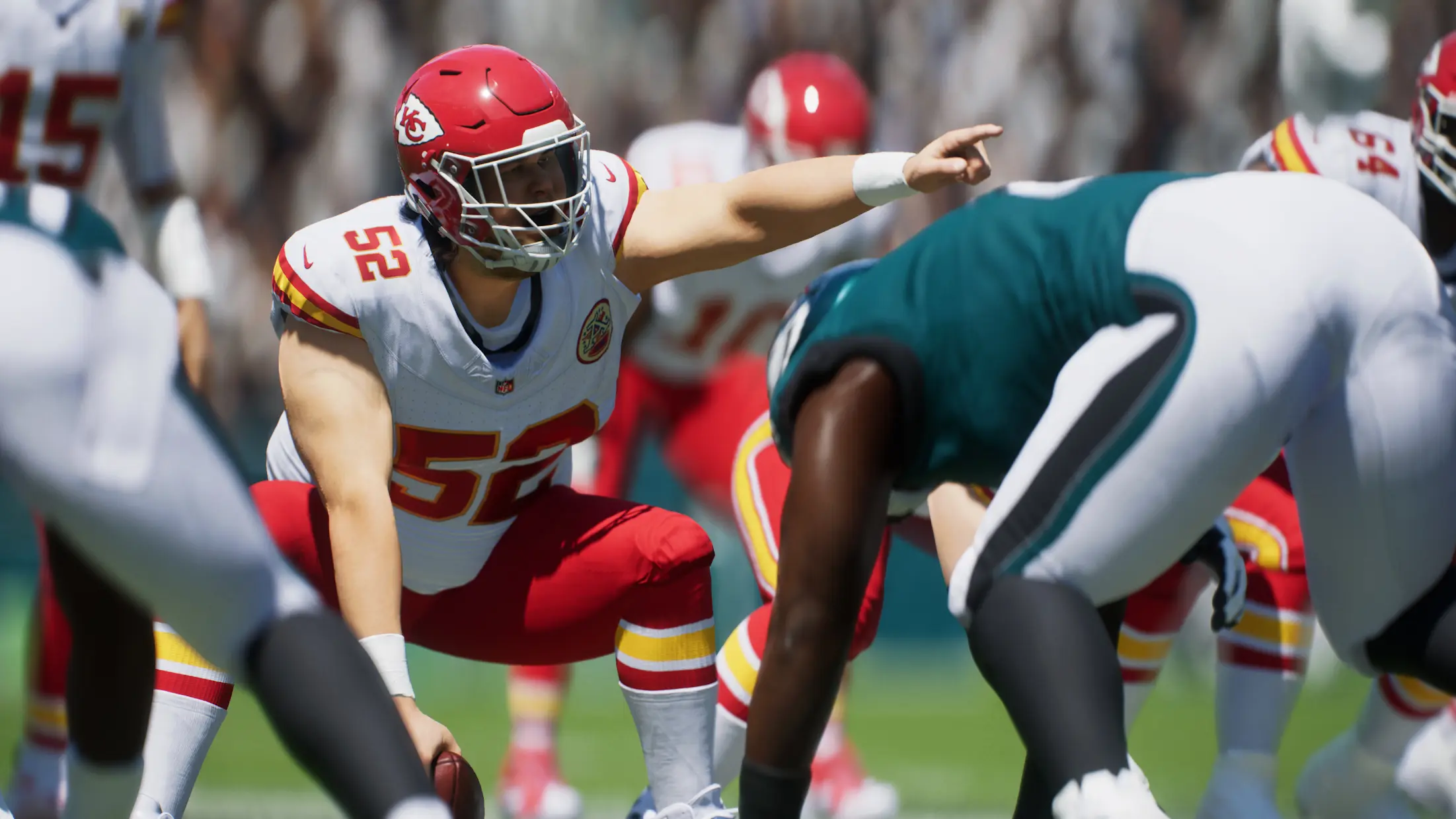 Two teams face off at the beginning of a play in Madden NFL 25. One player Squats and points with one hand while his other touches the ball on the ground.