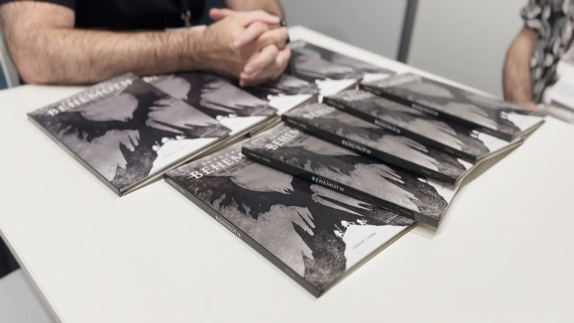 Several copies of the Skydance's Behemoth graphic novel are laid on a table. The front art shows several figures standing on a hill while the outline of a large winged monster is behind them.