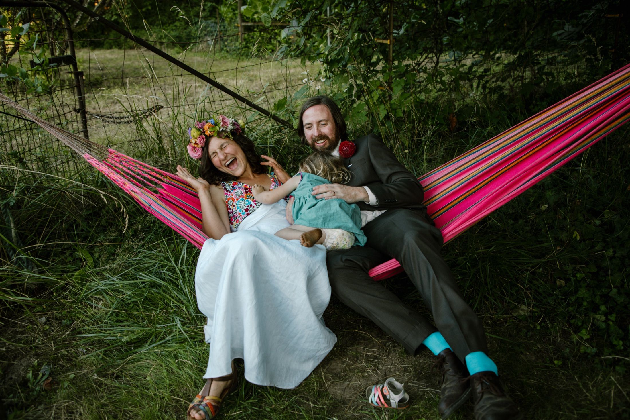 Melissa, Dave, and their child laughing in a hammock at their backyard wedding.