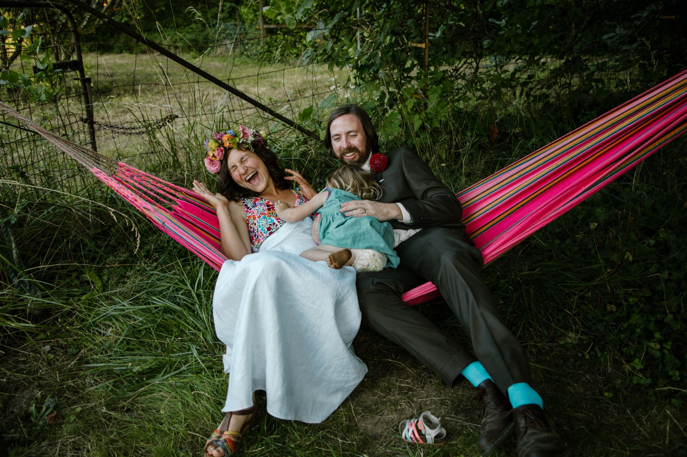 Melissa, Dave, and their child laughing in a hammock at their backyard wedding.