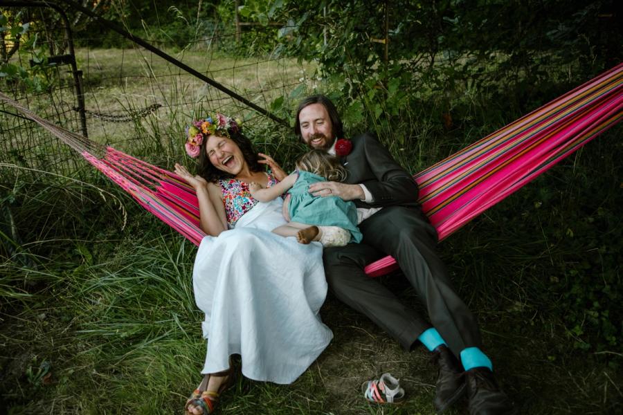 Melissa, Dave, and their child laughing in a hammock at their backyard wedding.