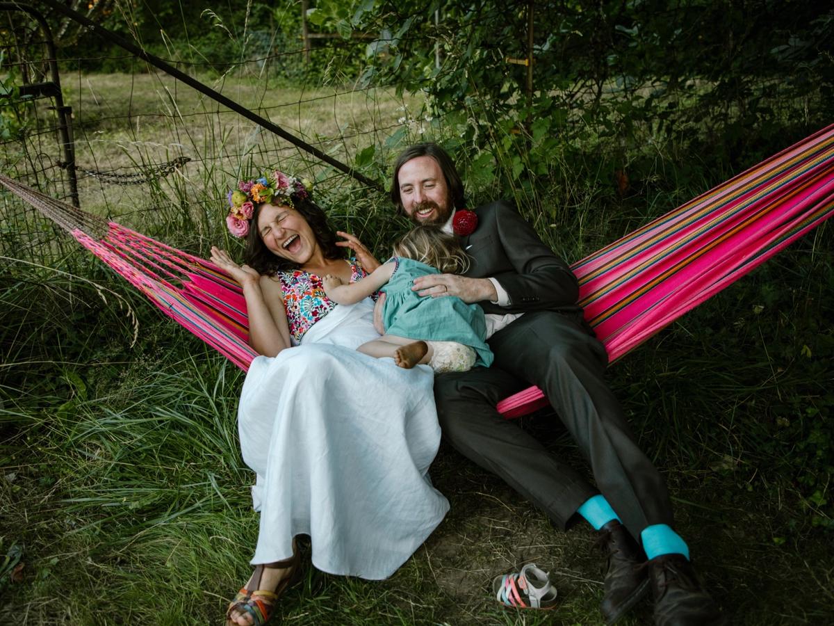 Melissa, Dave, and their child laughing in a hammock at their backyard wedding.