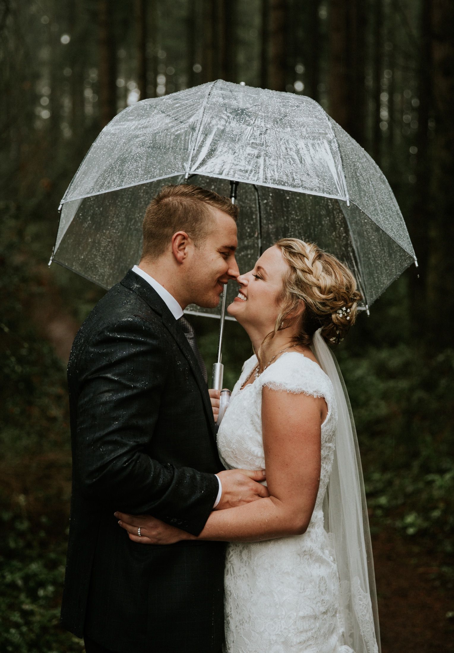 Tijs and Julie under a clear umbrella in the rain, foreheads touching.