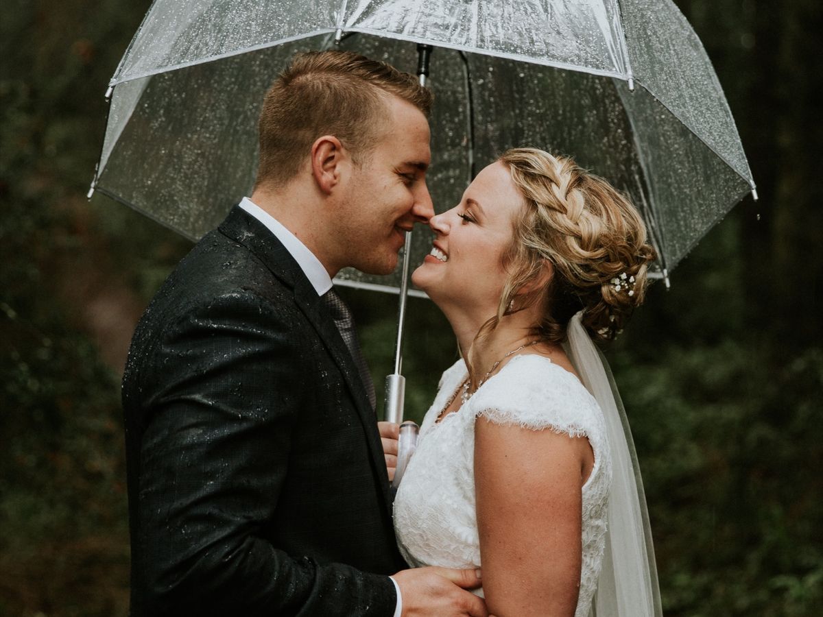 Tijs and Julie under a clear umbrella in the rain, foreheads touching.