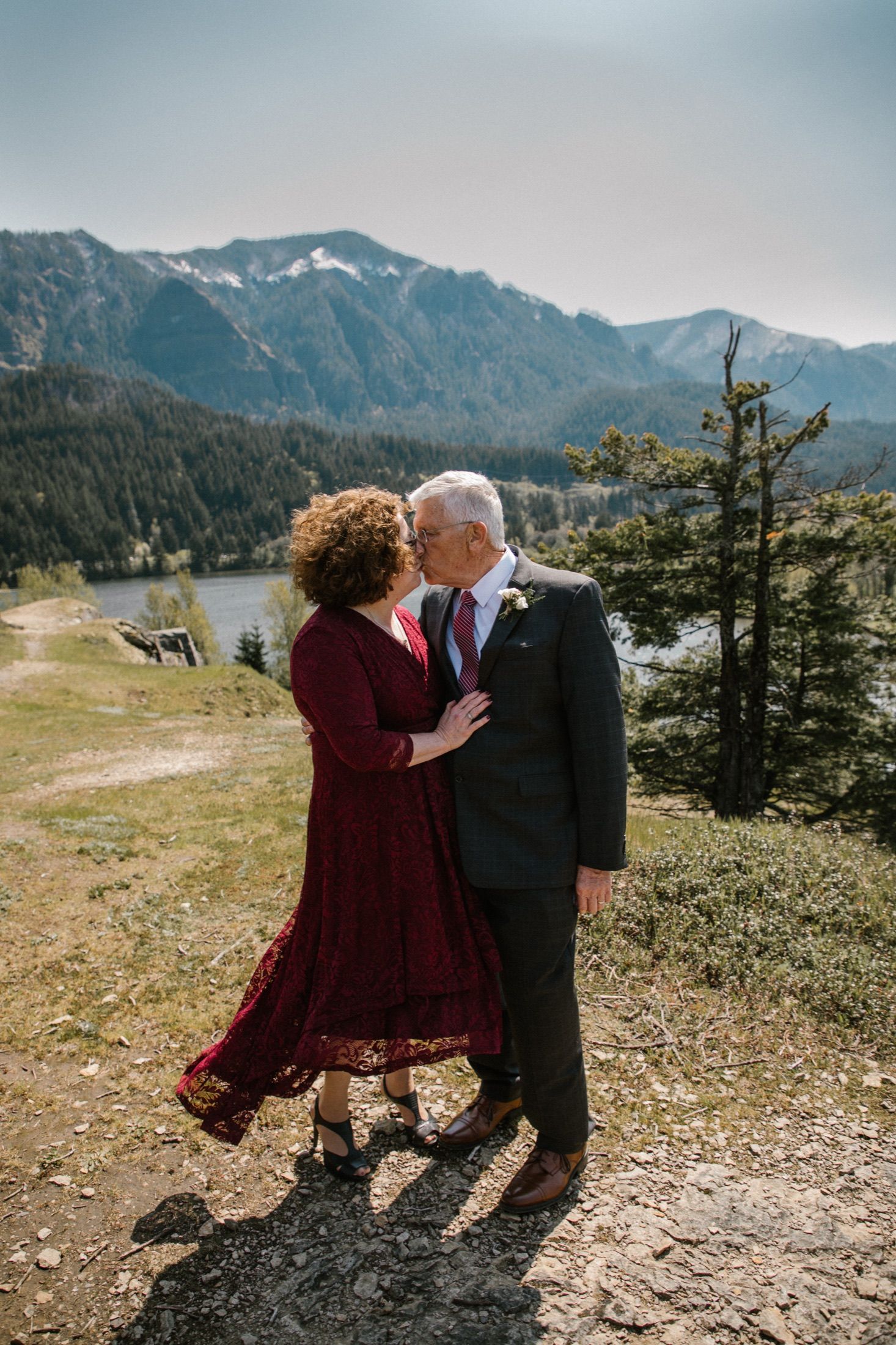 Yvette in a red dress and Dennis kissing on a mountain ridge.