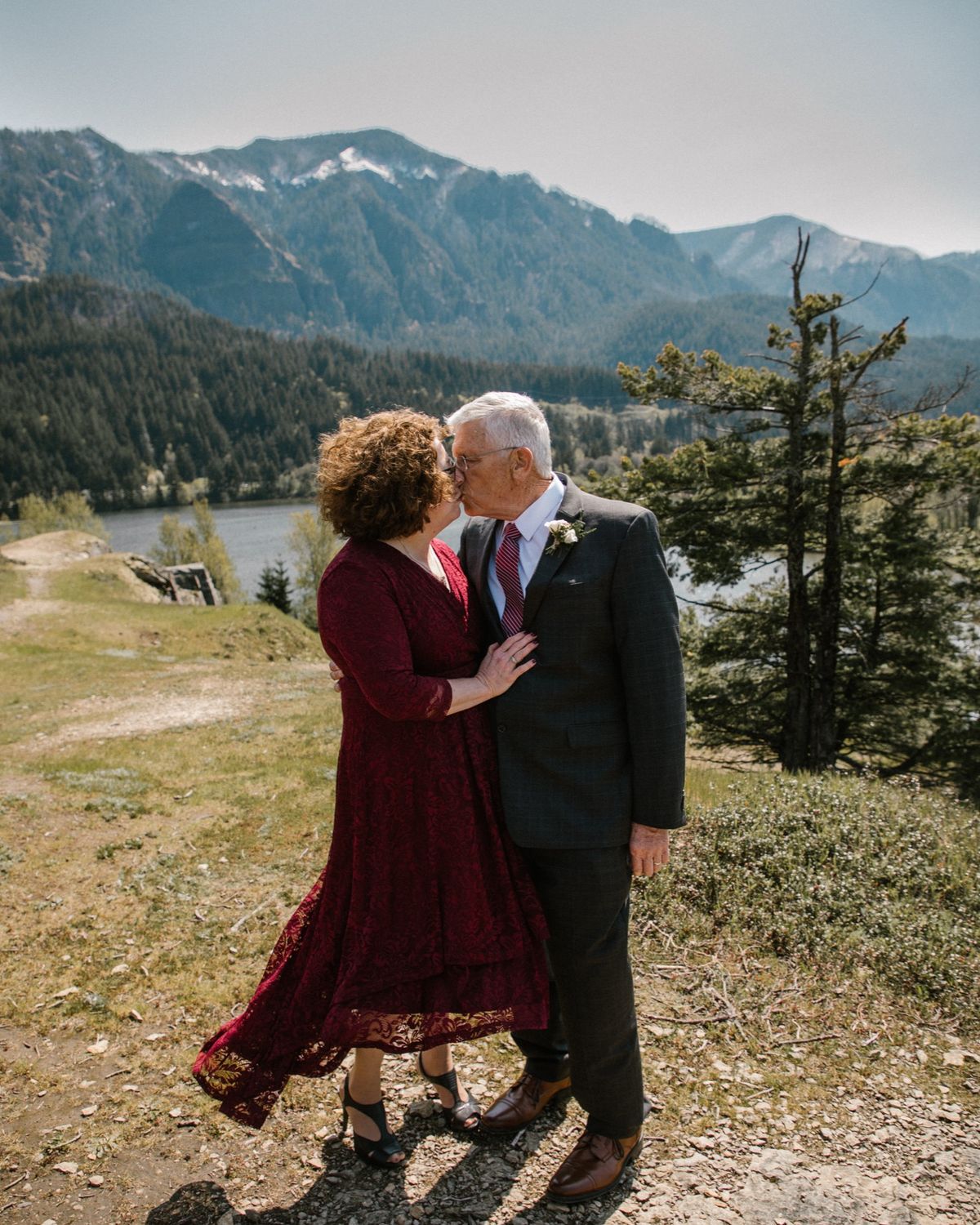 Yvette in a red dress and Dennis kissing on a mountain ridge.