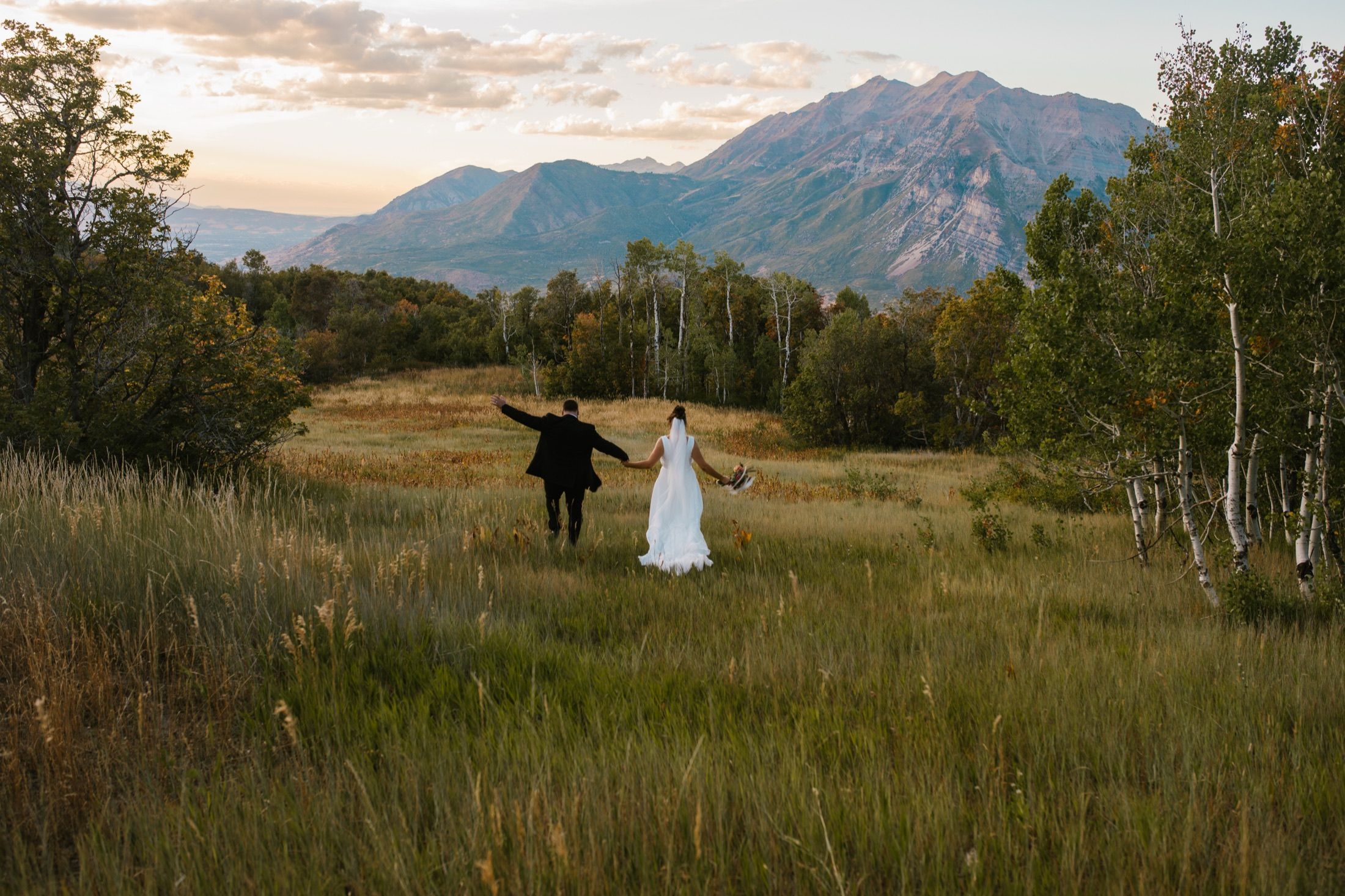 Mackey and Haylee running through a golden field with mountains behind them.