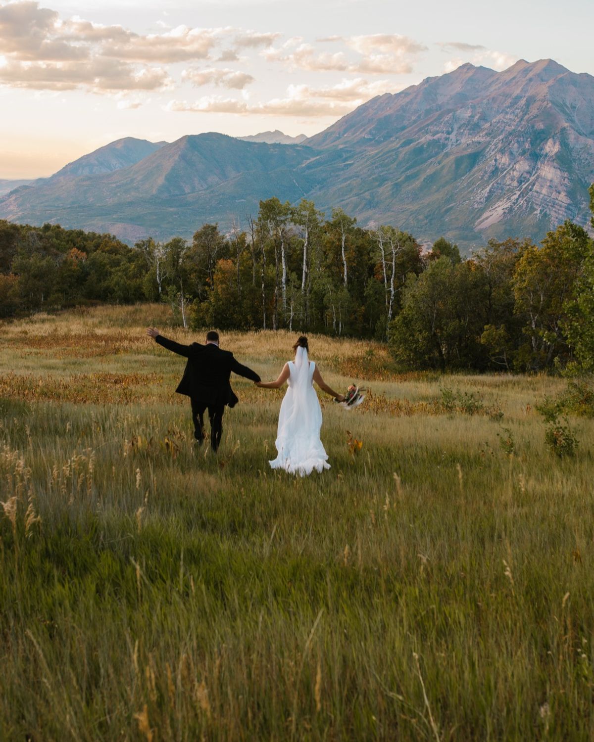 Mackey and Haylee running through a golden field with mountains behind them.