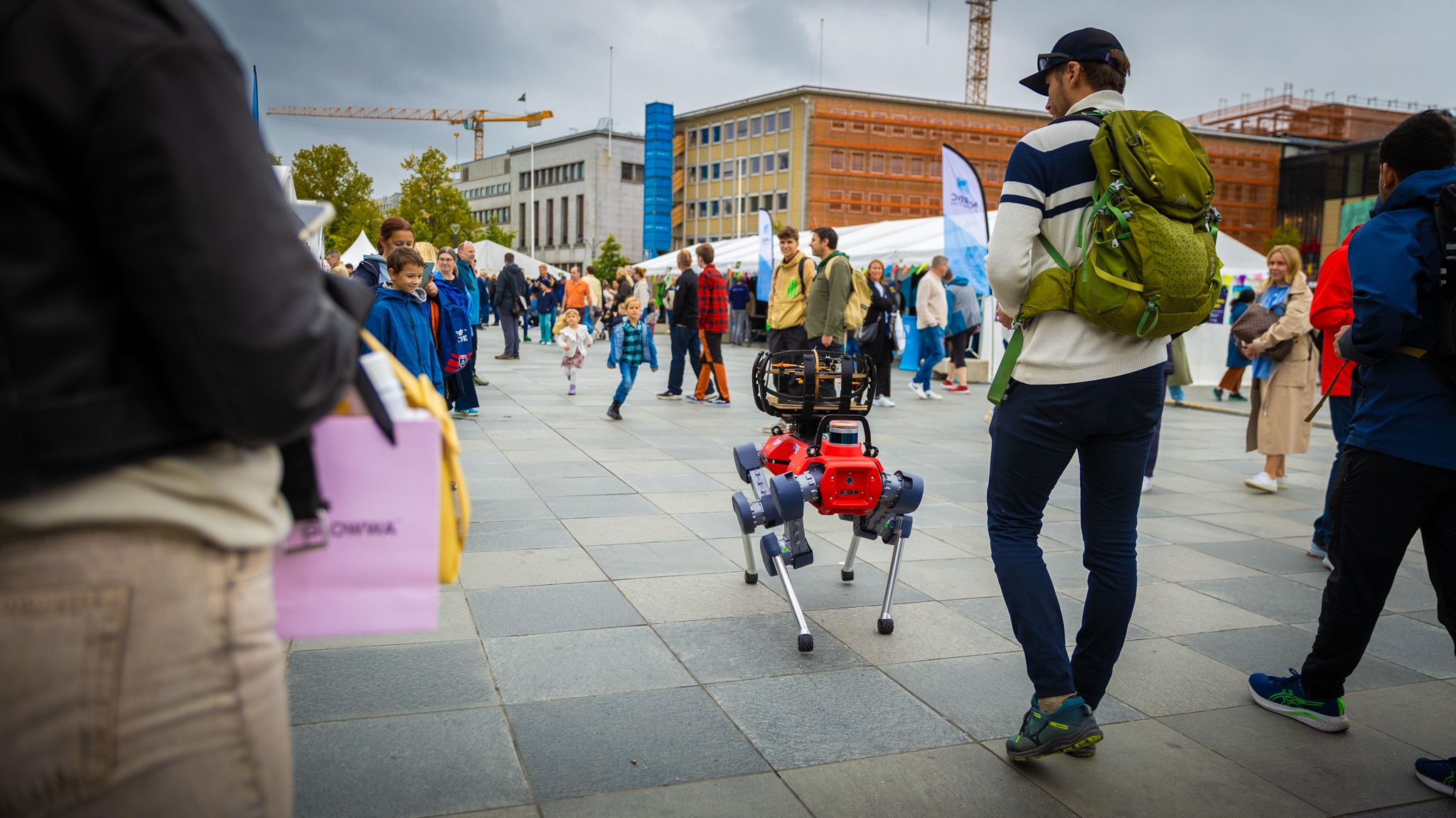 A four-legged robot walking among visitors on a busy city square during a tech event