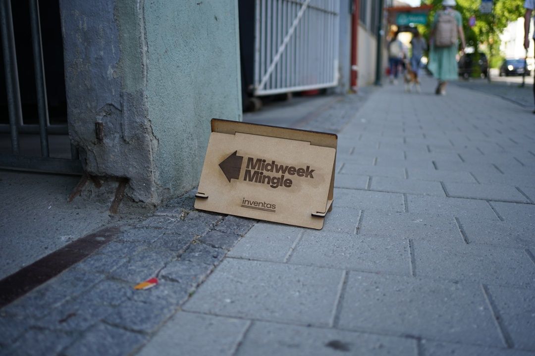 A wooden Midweek Mingle sign on a pavement pointing to the entrance