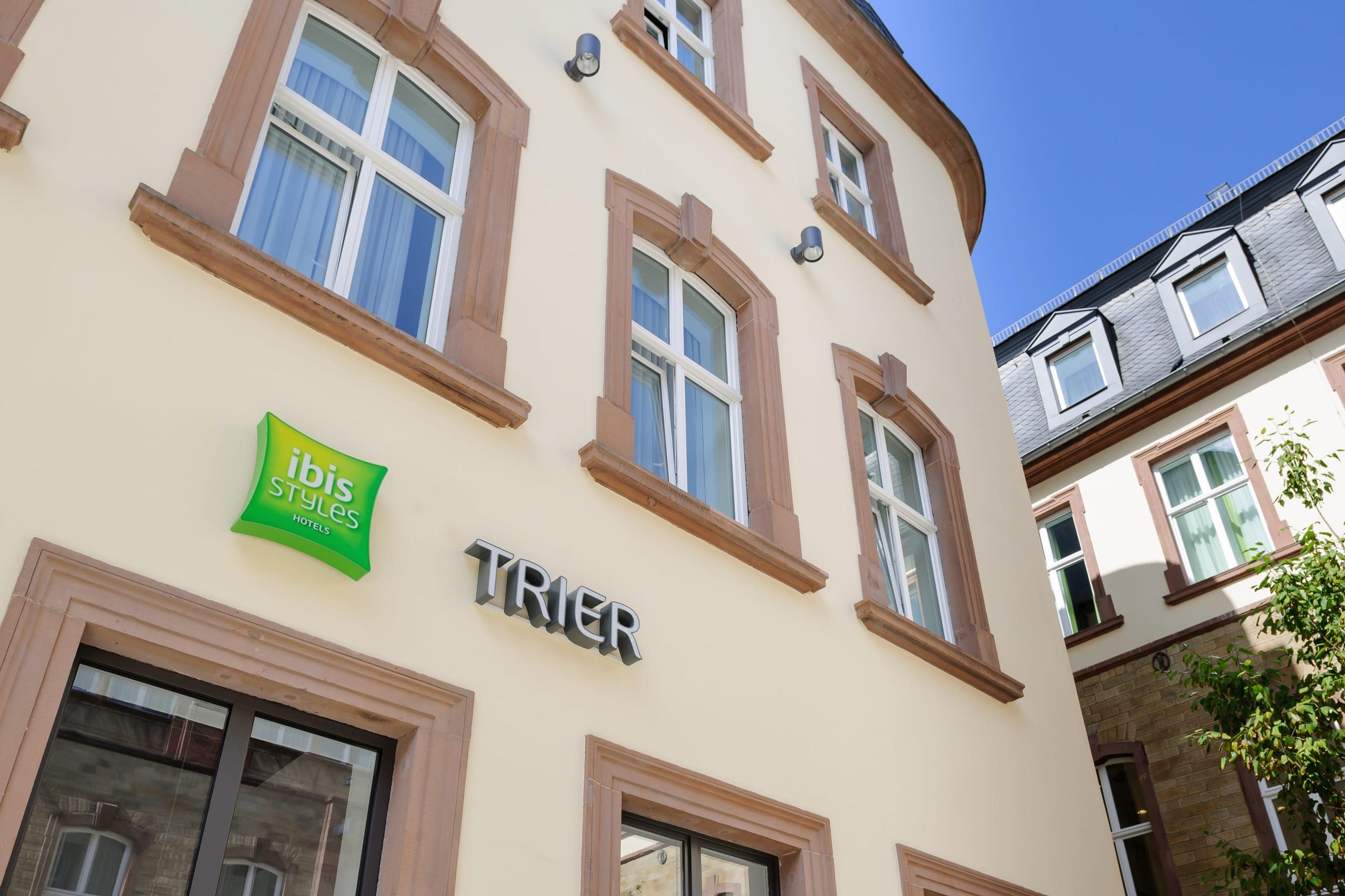 Fassadendetail mit grünem ibis Styles "TRIER"-Schriftzug