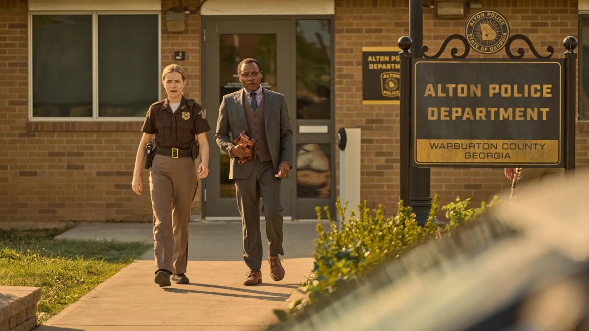 Willa Fitzgerald as Roscoe Conklin and Malcolm Goodwin as Oscar Finlay walk out of the Alton Police Department in Georgia, Finlay carrying his shoulder holster in one hand.