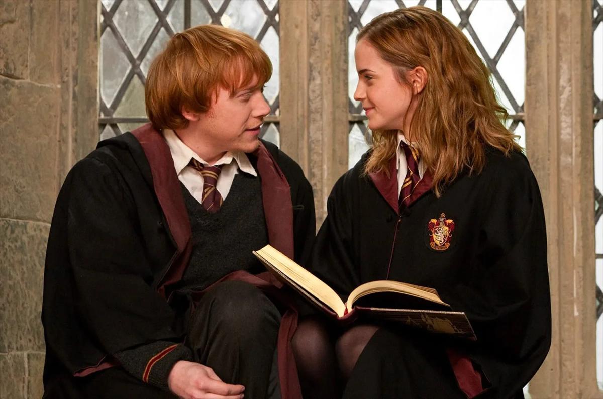 Rupert Grint as Ron Weasley and Emma Watson as Hermione Granger sitting together over an open book