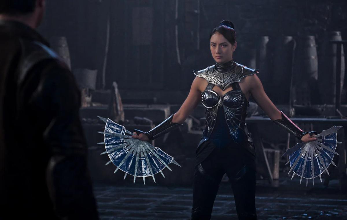 Adeline Rudolph as Kitana in silver armour, holding her bladed steel fans open at her sides.