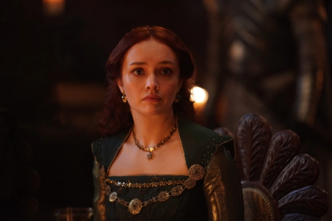 Alicent Hightower seated in a dark green gown, looking off to one side with a guarded expression