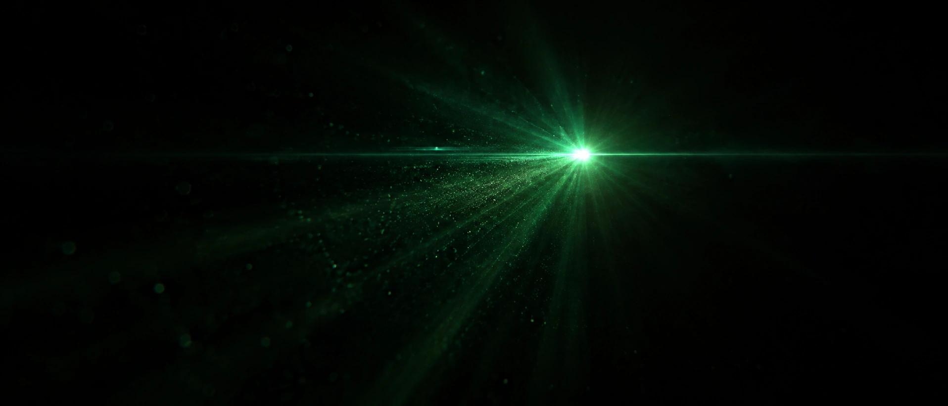 A single point of green light in darkness, casting rays through drifting particles.