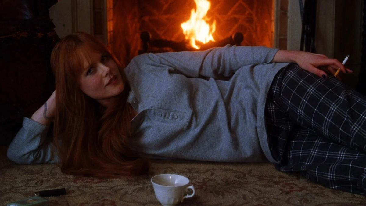 Nicole Kidman as Gillian Owens lying on the floor in front of a lit fireplace, holding a cigarette.