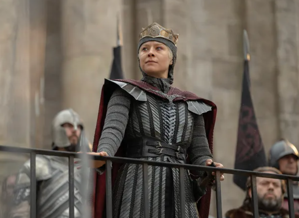 Rhaenyra in mail and a crown standing at a railing above the sept steps, guards on either side of her