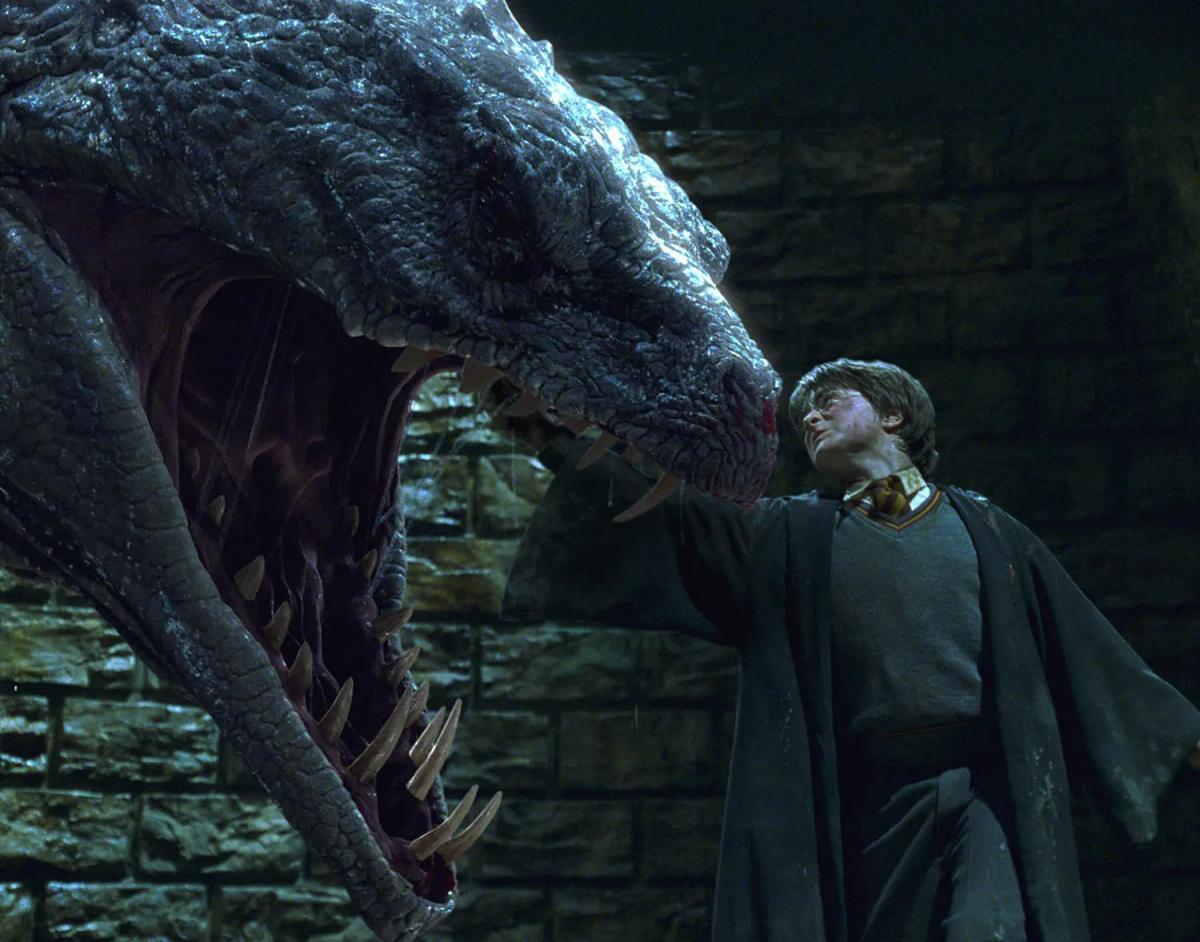 Harry Potter (Daniel Radcliffe) stands with one arm raised beside the open jaws of the basilisk in the Chamber of Secrets.