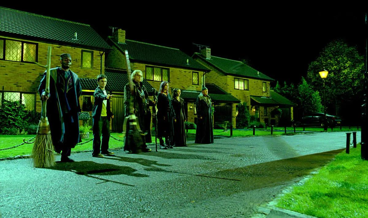Members of the Order of the Phoenix stand with broomsticks on a quiet suburban street at night.