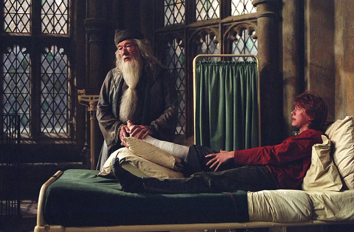 Michael Gambon as Albus Dumbledore beside Rupert Grint as Ron Weasley and his bandaged leg in the hospital wing