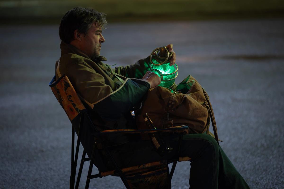 Kyle Chandler as Hal Jordan sitting outdoors at night, holding a glowing green power battery lantern in both hands.