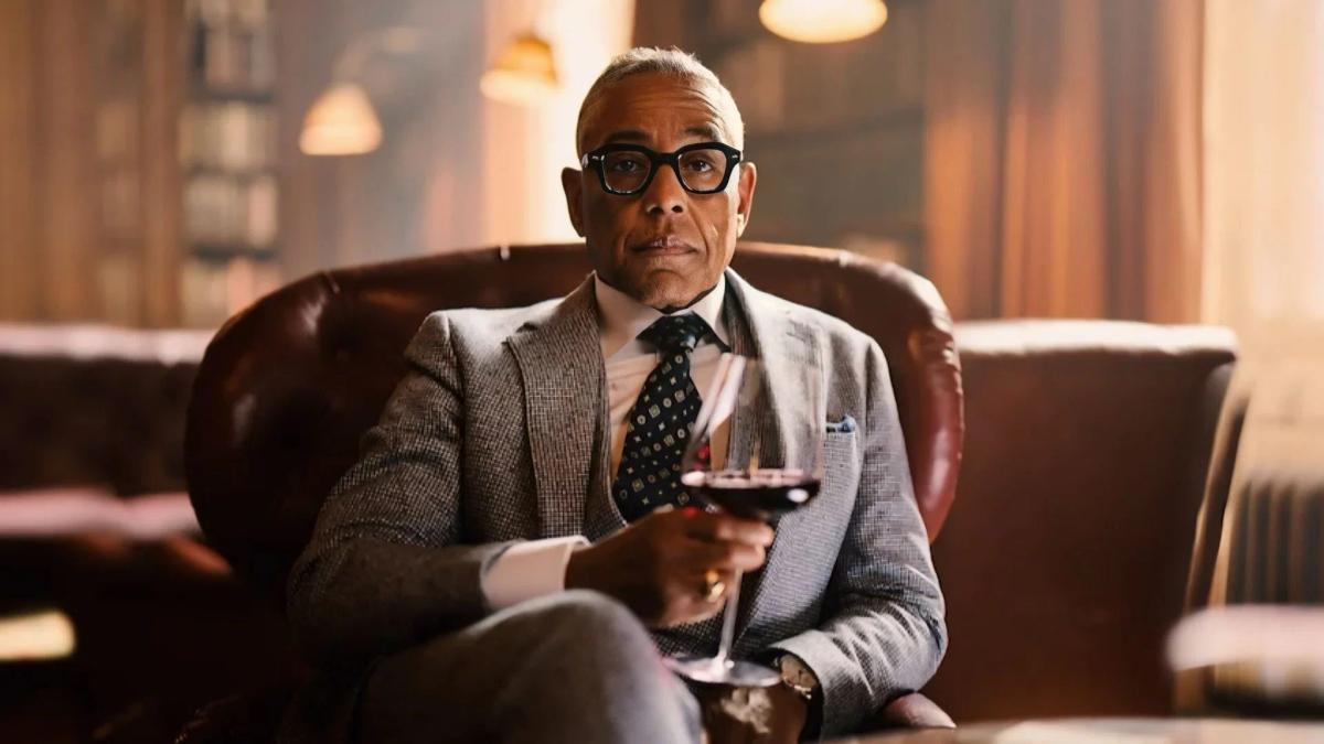 Giancarlo Esposito as Stanley Johnston, sitting in a leather armchair with a glass of red wine.