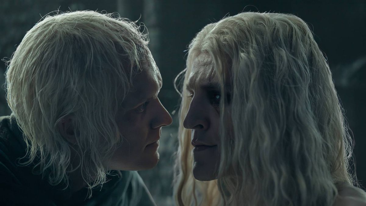 Two silver-haired men face to face in near-darkness, inches apart, one looking down at the other