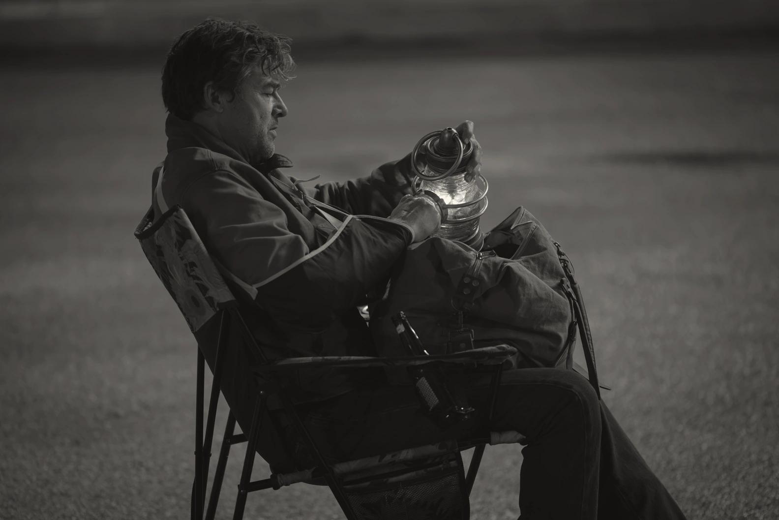 Kyle Chandler as Hal Jordan sitting alone at night holding a power battery lantern, shown in a black and white treatment.