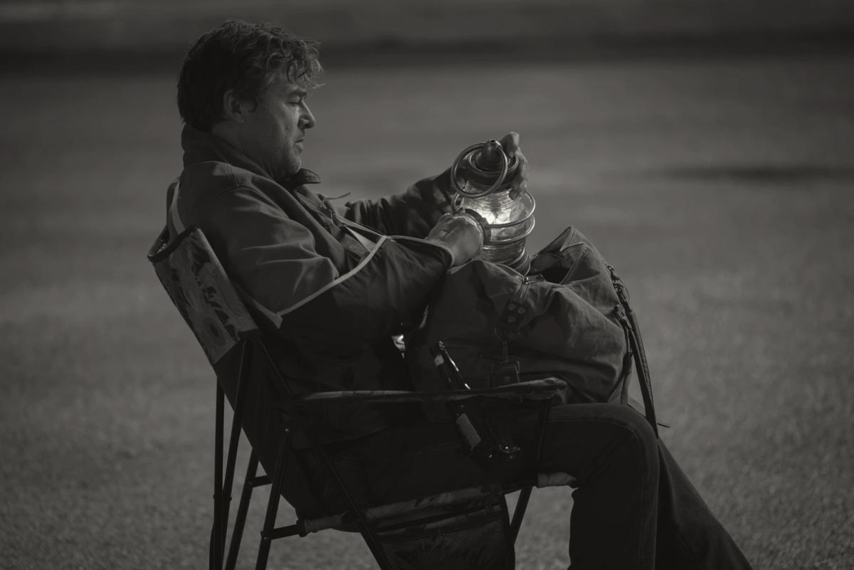 Kyle Chandler as Hal Jordan sitting alone at night holding a power battery lantern, shown in a black and white treatment.