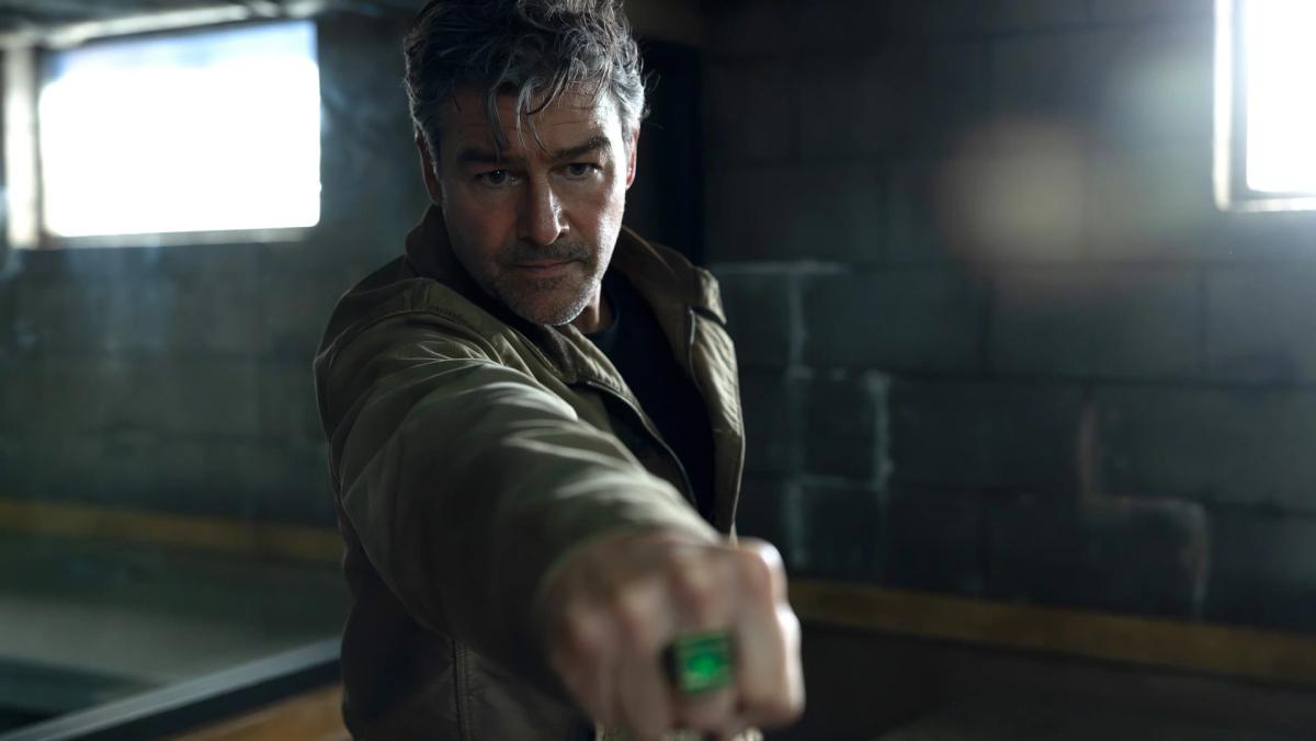 Kyle Chandler as Hal Jordan raising his green power ring in a darkened room in Lanterns episode 1
