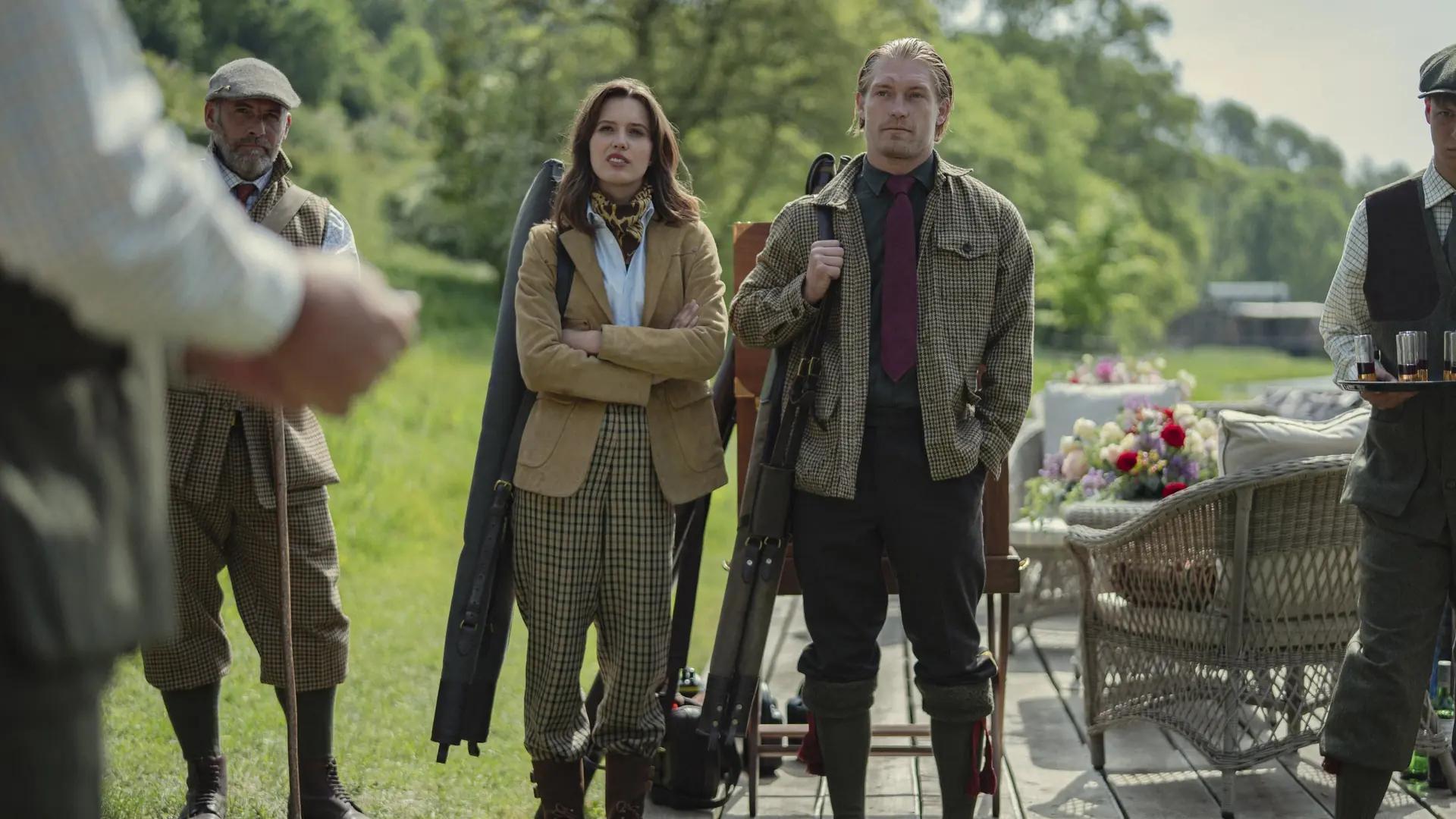 Guests in tweed shooting clothes standing with gun slips beside a wicker chair and a table of drinks on a lawn at Halstead.