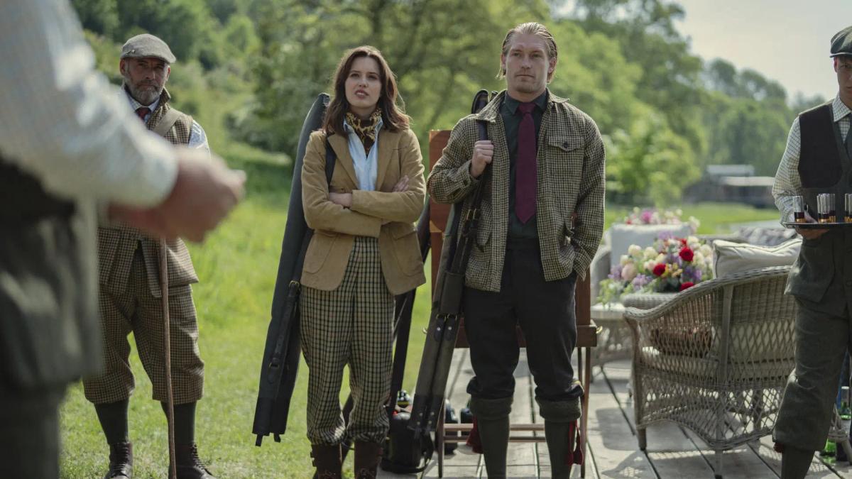 Guests in tweed shooting clothes standing with gun slips beside a wicker chair and a table of drinks on a lawn at Halstead.