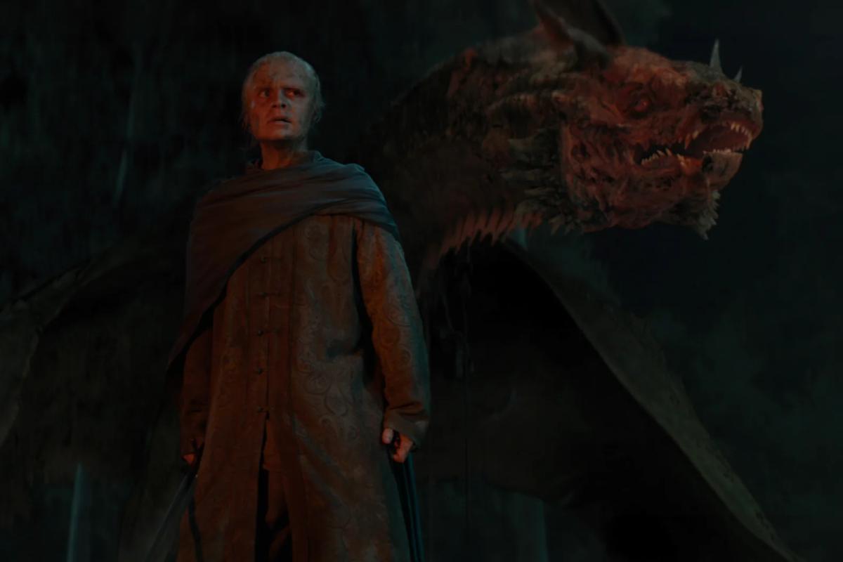 Tom Glynn-Carney as Aegon II Targaryen standing in front of the dragon Sunfyre in darkness
