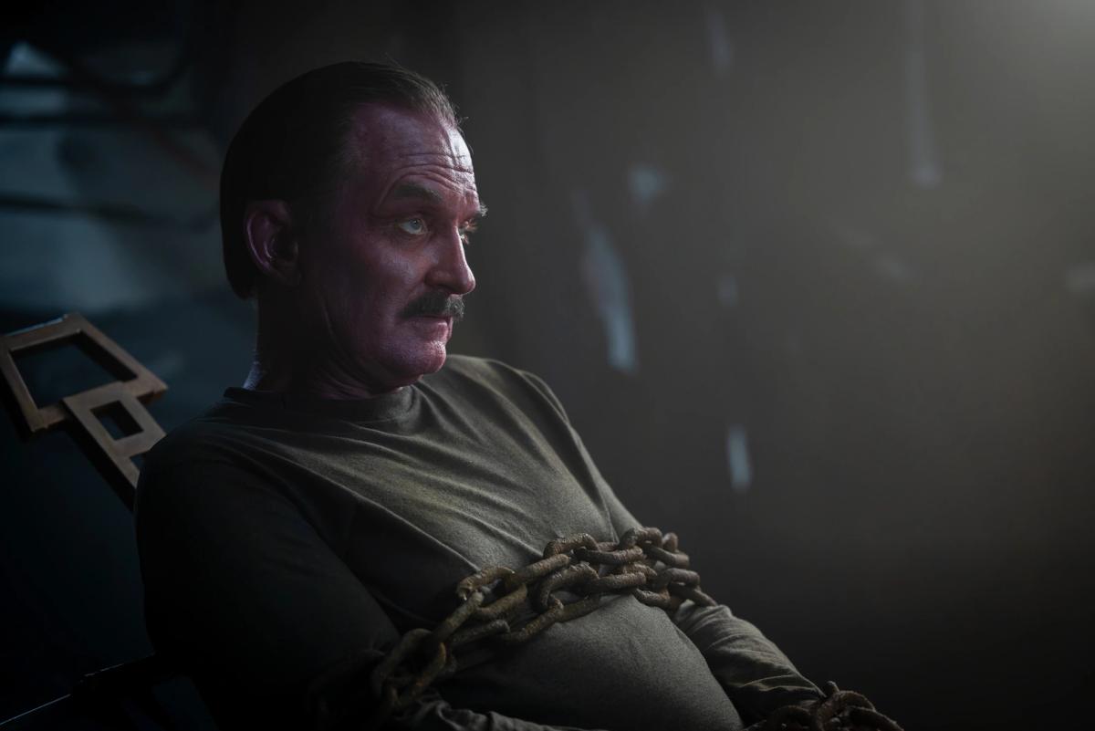 Ulrich Thomsen as Sinestro, rusted chains wrapped across his chest, seated in a dark room.
