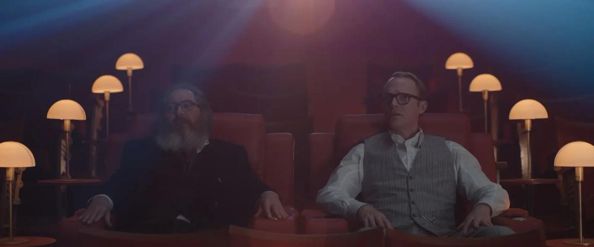 James Spader as Ultron and Paul Bettany as Vision sit side by side in red cinema seats in VisionQuest