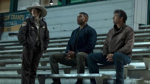 Kelly Macdonald, Aaron Pierre and Kyle Chandler on the bleachers at the Rushville football field in Lanterns episode 1