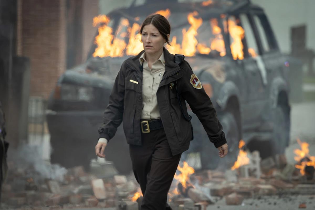 Kelly Macdonald as Sheriff Kerry Kane walking through Rushville as vehicles and rubble burn around her.
