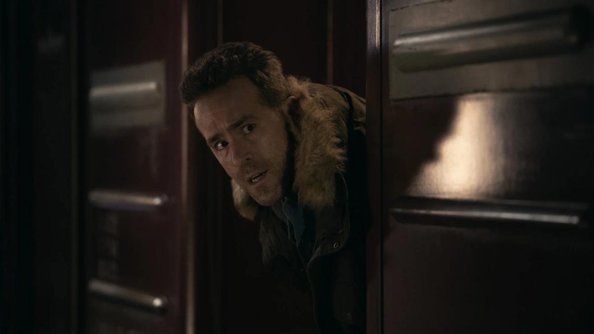 Ryan Reynolds as Troy Kelly leaning out from behind a doorway in a dim wood-panelled corridor