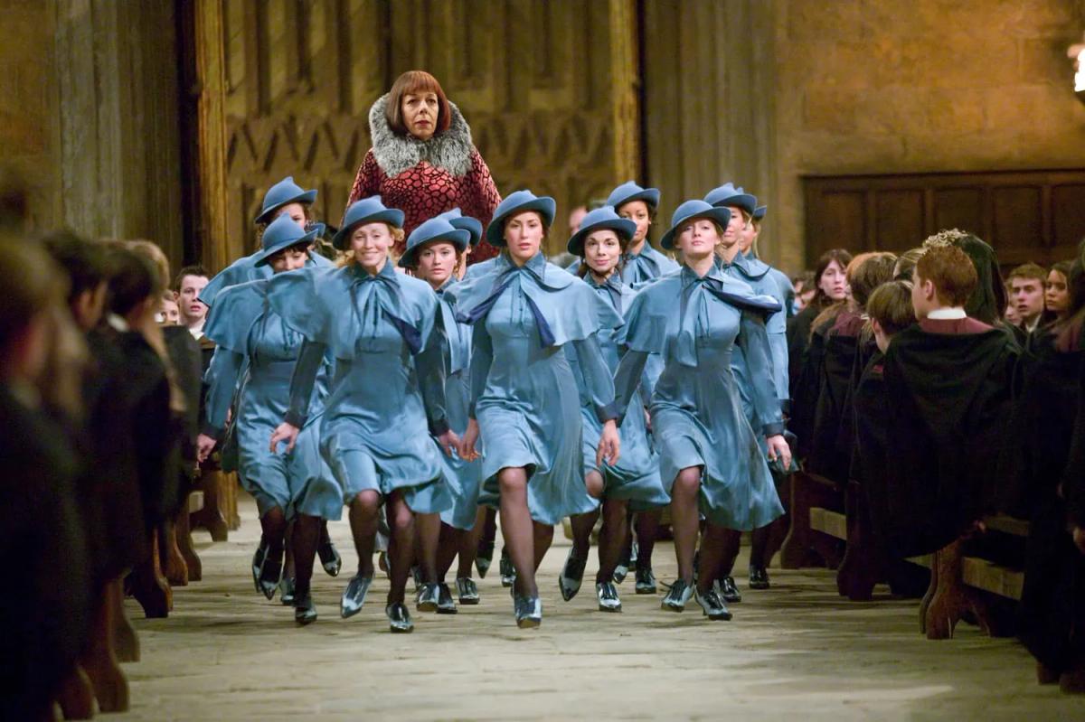 The Beauxbatons delegation, in pale blue uniforms and hats, walks in formation down the Great Hall between the watching house tables.