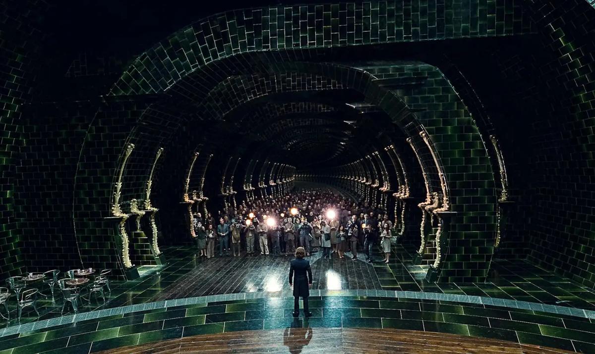 A lone figure stands at one end of the vast tiled Ministry atrium while a crowd with lights is gathered at the far end of the hall.