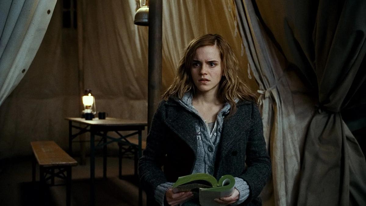 Emma Watson as Hermione Granger holding a book at the tent entrance during the Horcrux hunt