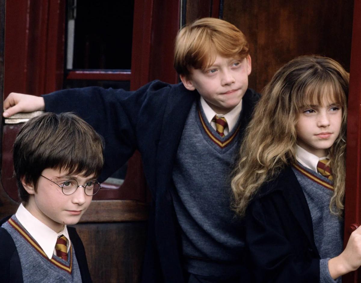 Harry Potter (Daniel Radcliffe), Ron Weasley (Rupert Grint) and Hermione Granger (Emma Watson) standing together in Gryffindor uniform.