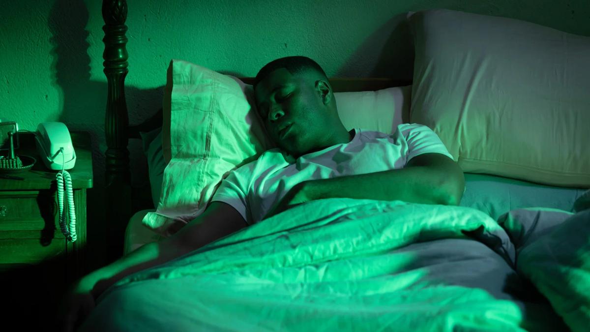 J. Alphonse Nicholson as John Stewart Sr. asleep in bed, the room flooded with green light from a power ring arriving.