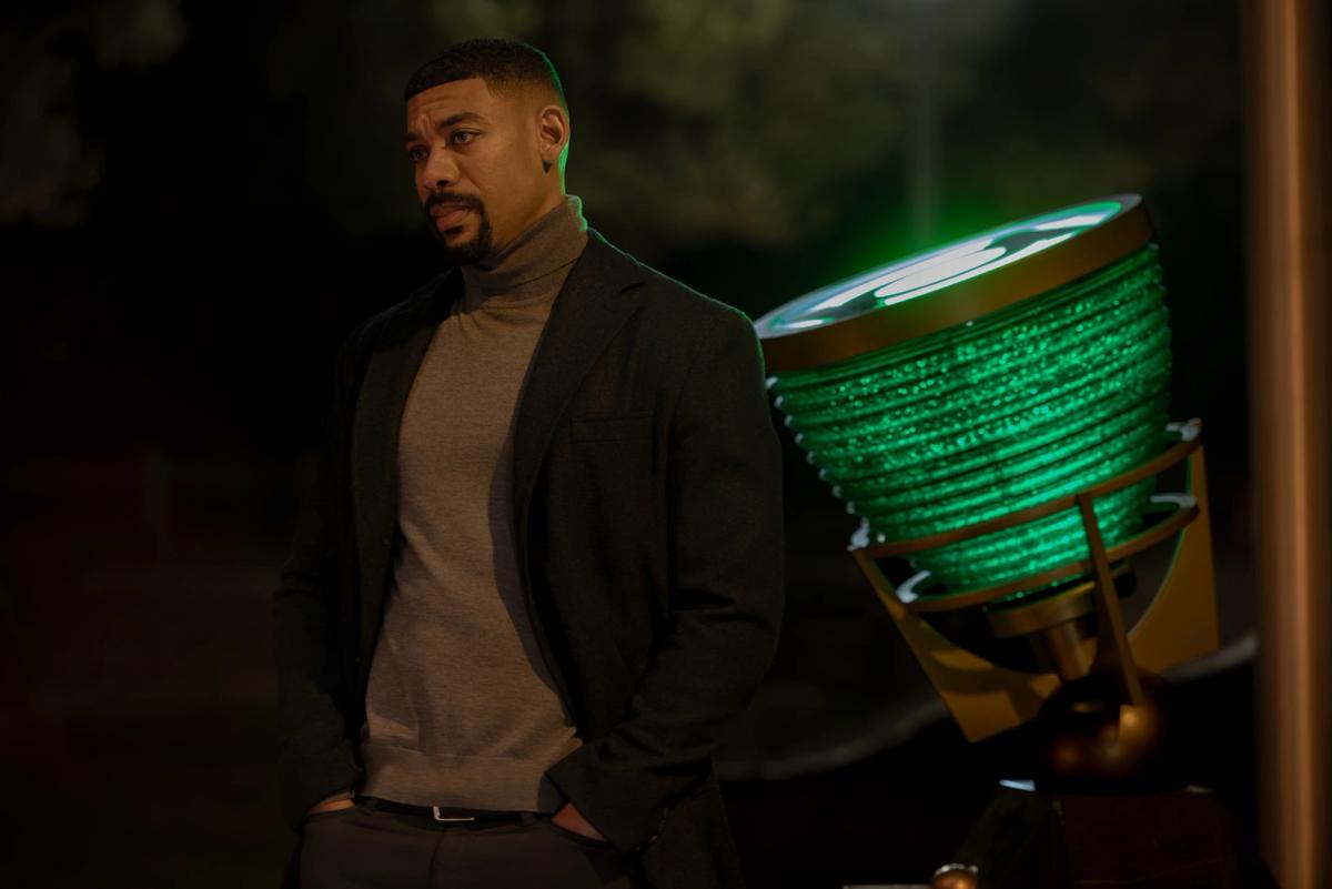 Aaron Pierre as John Stewart standing at night beside a large green-lit beacon in the centre of Rushville.