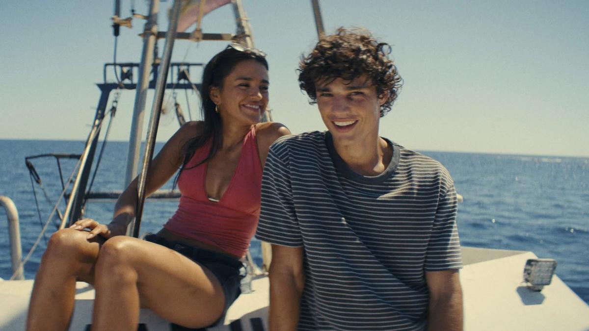 Maia Reficco as Oriah "Ry" Pera laughing beside Fernando Lindez as Julián García on a boat out at sea.