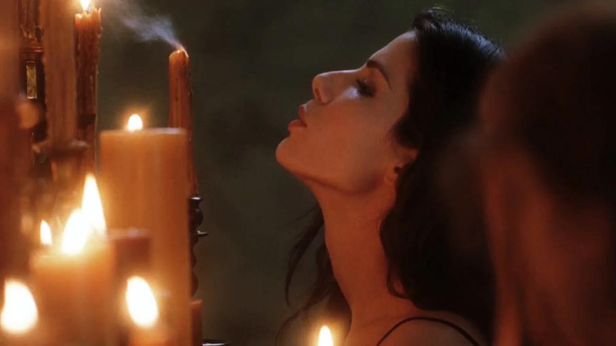 Sandra Bullock as Sally Owens leaning towards a bank of candles in the Owens house, one of them smoking.